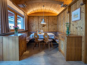 Ein Holzinterieur mit einem Essbereich, der einen Tisch und Stühle, ein Fenster mit Vorhängen sowie eine Holzkommode beinhaltet.