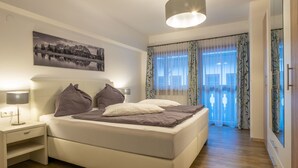 Ein modernes Schlafzimmer mit Bett, Nachttischen, einer Hängeleuchte, einem Gemälde an der Wand und Blick durch das Fenster.