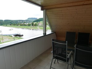 Ein Balkon mit Blick auf einen Fluss, ein Boot und eine hügelige Landschaft.