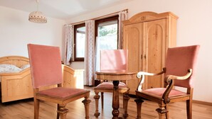 A room with a wooden bed, two upholstered chairs, a wooden table, and a wooden wardrobe.