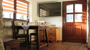 A room with a wooden desk, a chair, a television mounted on the wall, and a wooden door with glass panels. - Apartment Kontor by Interhome (Marschacht)