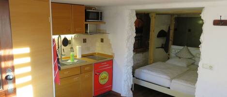 A compact room with a kitchenette, a bed, and a small table.