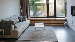 Ein modernes Wohnzimmer mit einer Couch, einem Couchtisch und einem großen Fenster mit Blick auf Bäume.