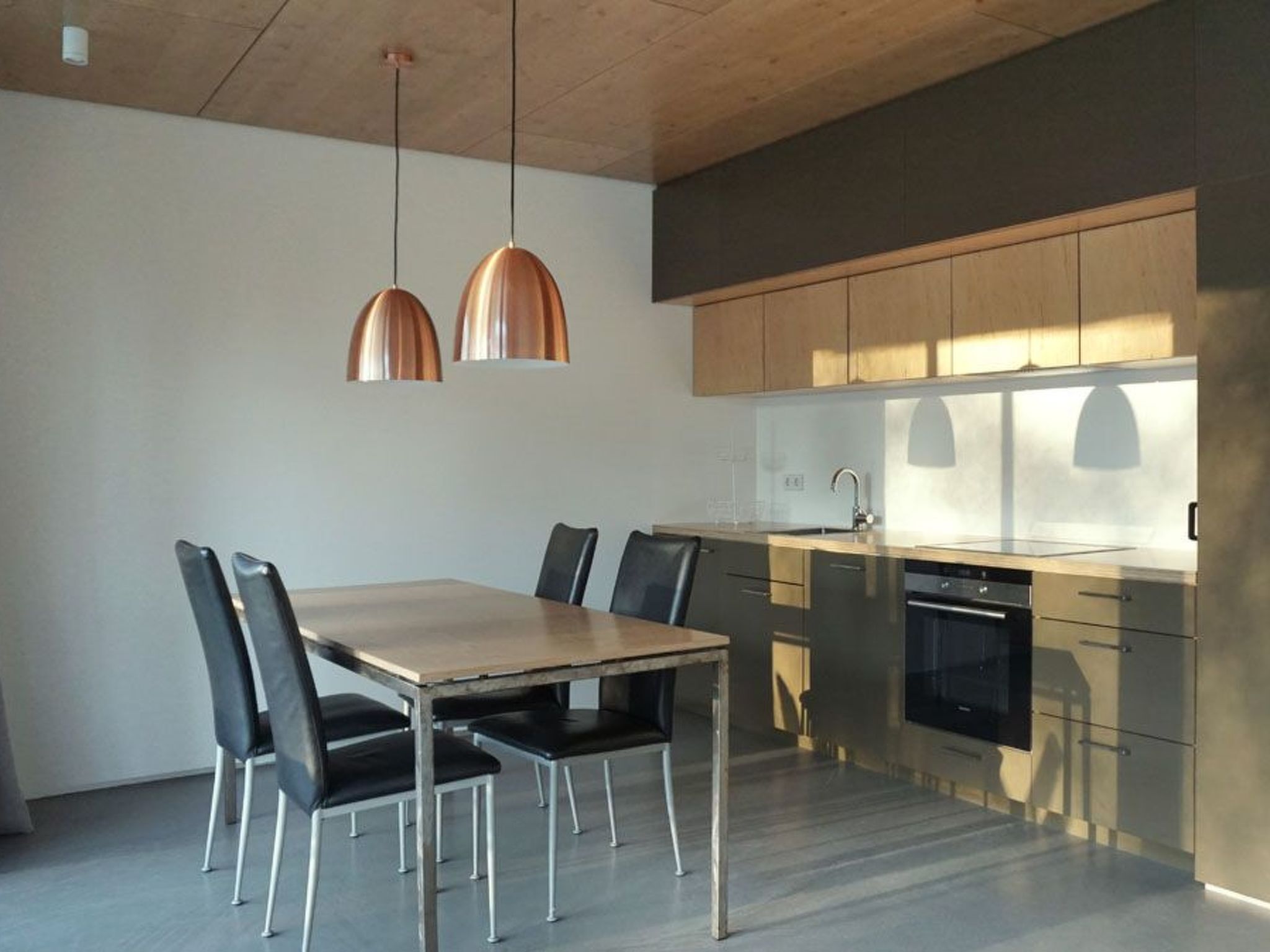 A modern kitchen with a wooden table and chairs, stainless steel appliances, and pendant lights.