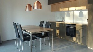 Eine moderne Küche mit Holztisch und -stühlen, Edelstahlgeräten und Pendelleuchten.