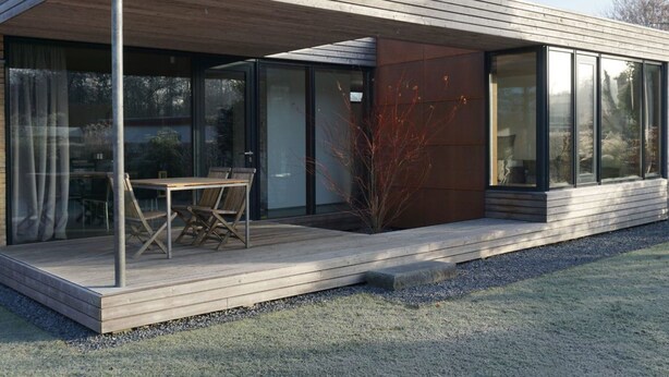 Ein modernes Haus mit Holzterrasse, großen Glasfenstern und minimalistischem Design.