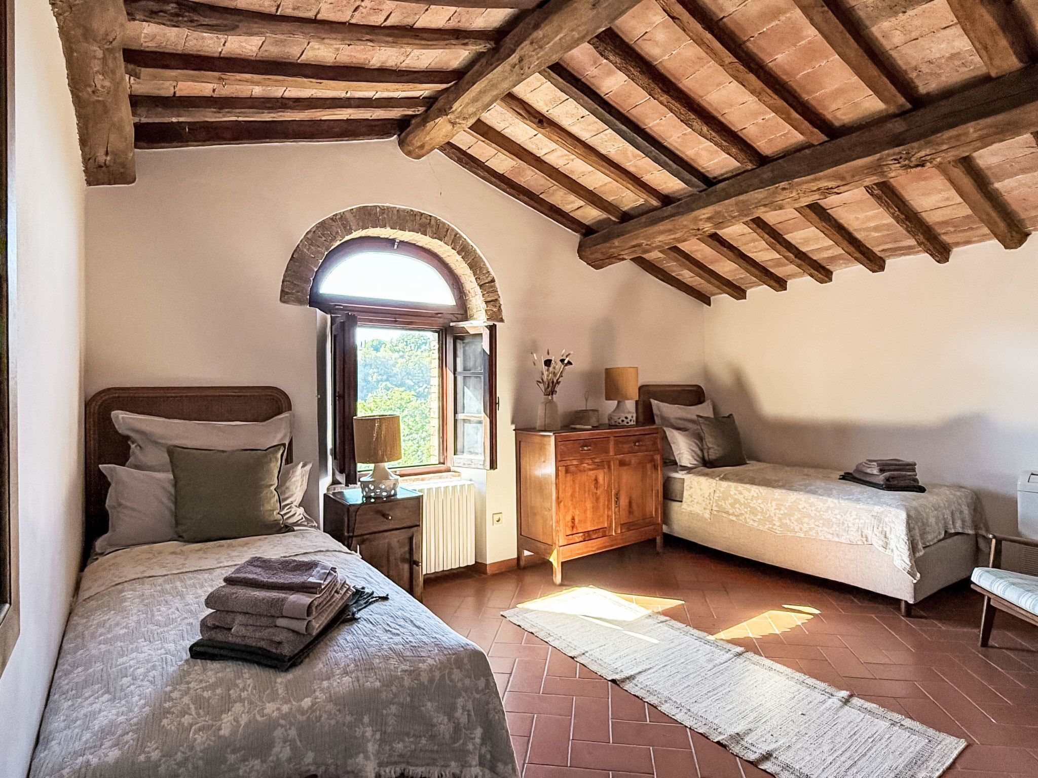 A bedroom with two beds, a wooden cabinet, a window with an arch, and a radiator.