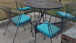 Eine Terrasse mit einem runden Metalltisch und vier Stühlen, jeder mit einem blauen Sitzkissen.
