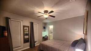 Ein Schlafzimmer mit Bett, Deckenventilator, Nachttischlampe, Kommode und Spiegel.