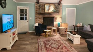 Ein Wohnzimmer mit Kamin aus Ziegelsteinen, einem Fernseher, einer Uhr und einem Deckenventilator.