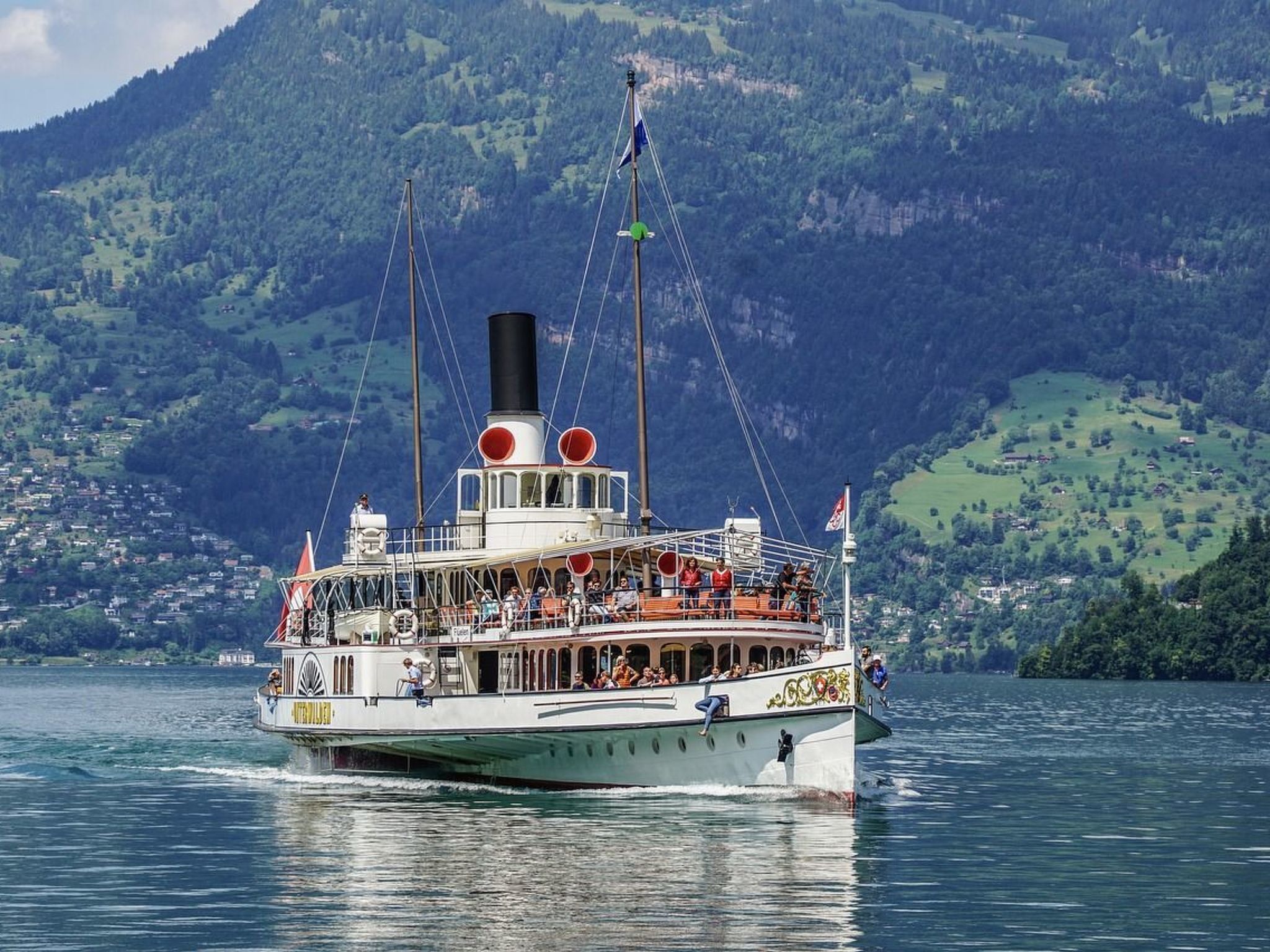 Un bateau à vapeur transportant des passagers sur le pont, entouré d’un paysage montagneux.