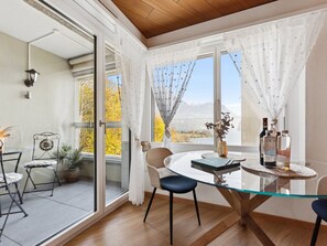 A modern dining area with a glass table, chairs, and a view of autumn foliage through large windows. - Lake View Studio by Interhome (Brunnen)