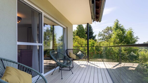 A balcony with two wicker chairs and a table, overlooking a lush green landscape. - Overlook Lodge by Interhome (Vöhl)