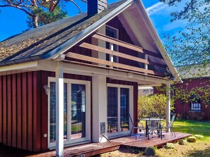 Une petite maison de plain-pied, dotée d’un toit en pente, de grandes fenêtres et d’une terrasse en bois aménagée avec du mobilier d’extérieur.
