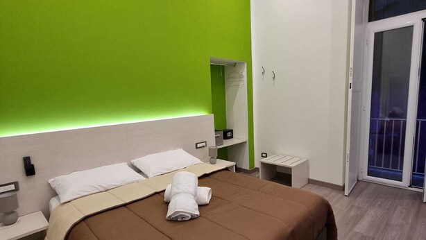 Une chambre d’hôtel moderne avec un grand lit, une table de chevet, une commode et un mur d’accent vert.