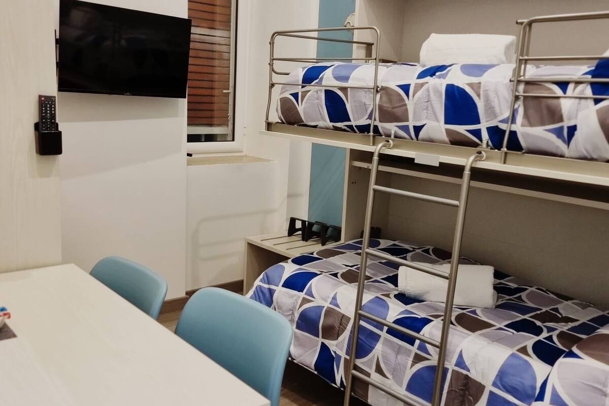 A dormitory room with bunk beds, a TV, a desk, and chairs.