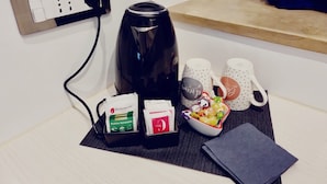 Un coin cuisine comprenant une machine à café, deux tasses, un bol de collations et une serviette en papier posée sur un set de table.