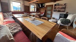 A cozy cabin interior with a wooden dining table, a sofa with a fur throw, and a television mounted on the wall. - Haus Schönblick by Interhome (Tannheim)
