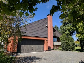 Ein modernes Haus mit dunklem Dach, einem Ziegelkamin und einer Garage.