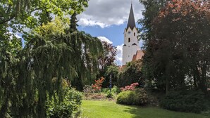 En trädgård med ett vitt kyrktorn och frodig grönska.