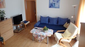Een woonkamer met een bank, een televisie, een tafel met een bloemenonderzetter, en een stoel.