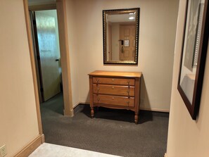 A hallway with a wooden dresser, a mirror, and a door. - Spacious 2-bedroom condo in beautiful Palm Harbor with ALL the amenities! (Palm Harbor)
