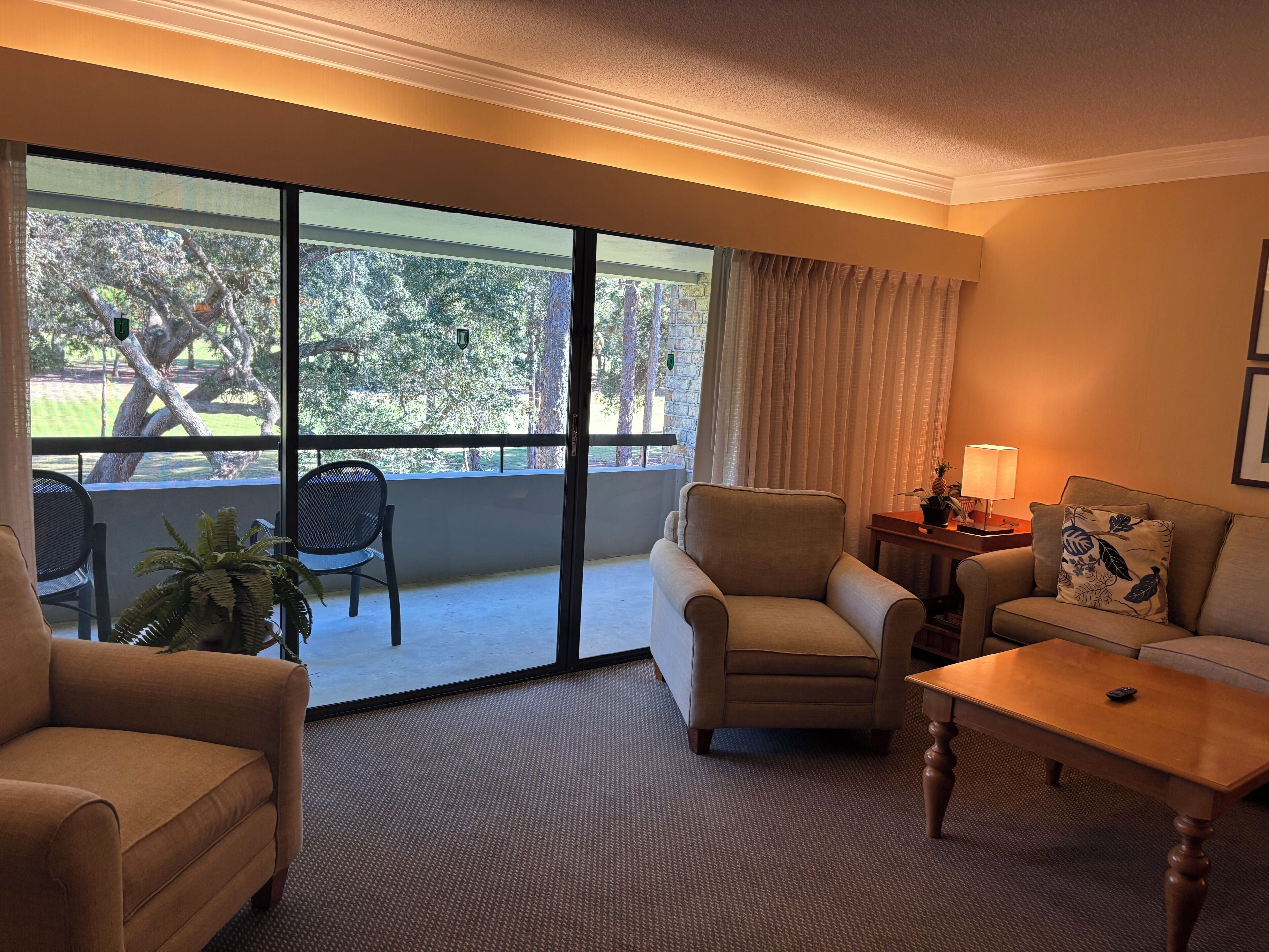 A hotel room with a balcony, a sofa, a chair, a table, and a lamp.