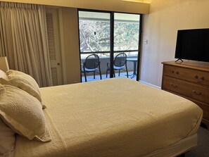 A hotel room with a bed, a dresser, a television, and a balcony with chairs. - Spacious 2-bedroom condo in beautiful Palm Harbor with ALL the amenities! (Palm Harbor)