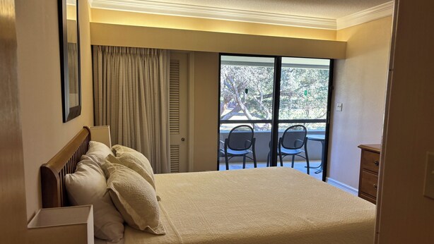 Ein Hotelzimmer mit einem großen Bett, Blick ins Freie durch eine Schiebetür und einem Balkon mit Sitzgelegenheiten.
