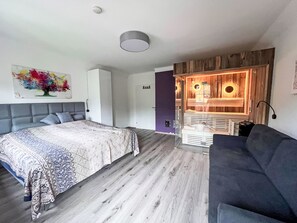 A modern bedroom with a bed, a grey sofa, a wooden wall unit, and a colorful abstract painting. - Apartment  by Interhome (Murau)
