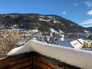 Un paese montano innevato con edifici residenziali e commerciali, una chiesa importante e un cielo azzurro limpido.