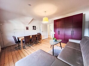 Een moderne woonkamer met een bank, een eettafel met stoelen, een klein bijzettafeltje en een grote kledingkast.