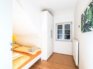 Een kleine, lichte kamer met een bed, een kledingkast en een raam.