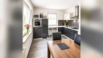 A modern kitchen with a dining area, featuring a wooden table and chairs, a built-in oven, and a window with a view.