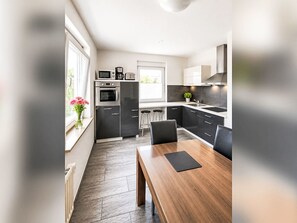 Et moderne køkken med spiseplads, med et træbord og stole, en indbygget ovn og et vindue med udsigt.