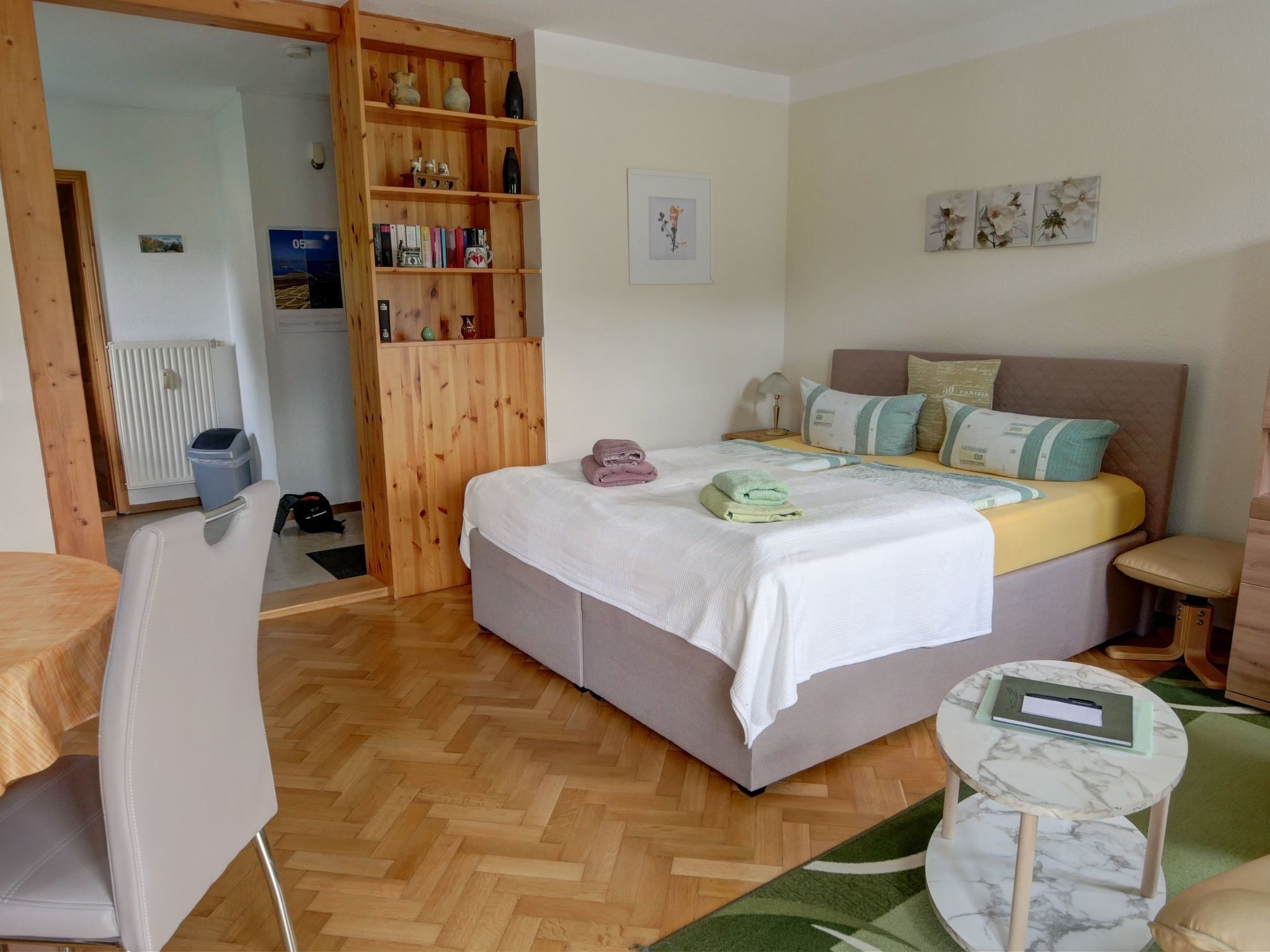 Un dormitorio con una cama, un armario de madera, una mesita redonda y una silla.