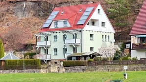 Et toetagers hus med rødt tag og solpaneler, beliggende nær et vandareal.