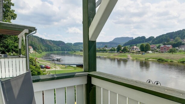 En balkon med udsigt over en flod, grønne bakker og bygninger i det fjerne.