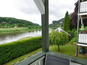 En vy från en balkong med utsikt över en flod, med ett hus och grönska i bakgrunden.