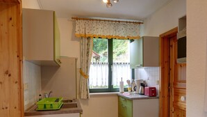 A compact kitchen with a window, wooden cabinets, a sink, and basic appliances. - Wohnung Barbarine by Interhome (Königstein)