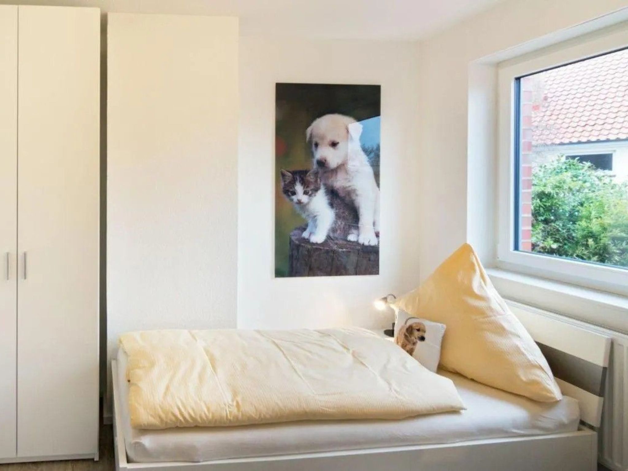 Een slaapkamer met een bed, een raam, een aan de muur hangend foto van een puppy en een kledingkast.