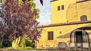 A yellow building with a stone facade, a small tower, and a patio with outdoor seating. - La Cisterna by Interhome (Volterra)
