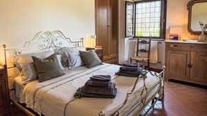 A bed with a metal frame, a wooden wardrobe, a window with a view, and a mirror on the wall. - La Cisterna by Interhome (Volterra)