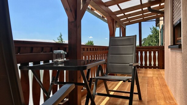 Une terrasse en bois avec un toit en verre, une table et une chaise.