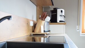 Une cuisine compacte équipée d’un évier en acier inoxydable, d’une machine à café et d’un bloc à couteaux posé sur le plan de travail.