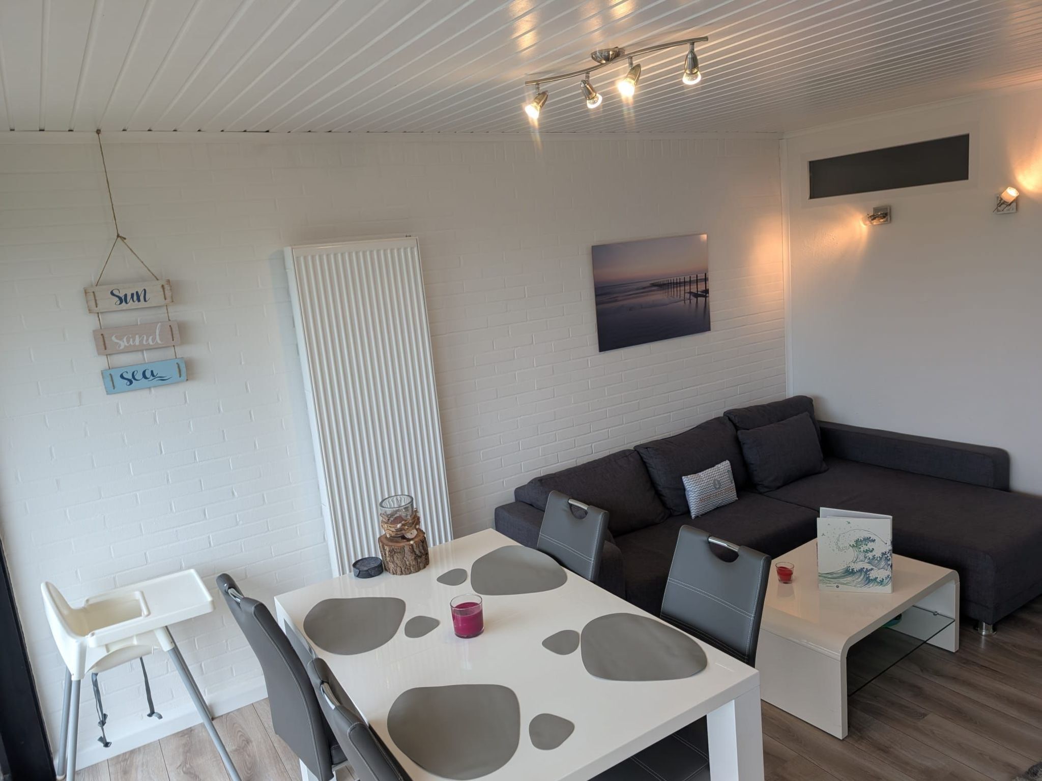 Ein modernes Wohnzimmer mit einem weißen Tisch, einem grauen Sofa und einem Fernsehgerät mit weißem Rahmen an der Wand.