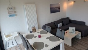 Ein modernes Wohnzimmer mit einem weißen Tisch, einem grauen Sofa und einem Fernsehgerät mit weißem Rahmen an der Wand.