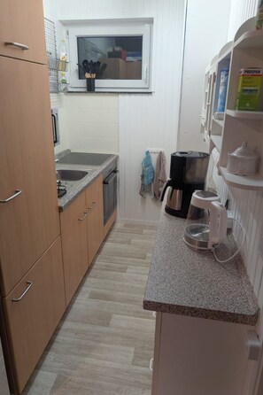 A compact kitchen with wooden cabinets, a granite countertop, a coffee maker, and a window above the sink. - Vacation home LouJa by Interhome (Burhave)