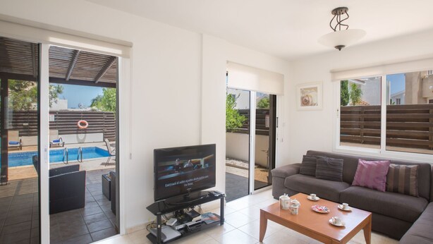 A living room with a TV, a sofa, a coffee table, and a pool view. - Ferienvilla Protaras 14 by Interhome (Protaras)