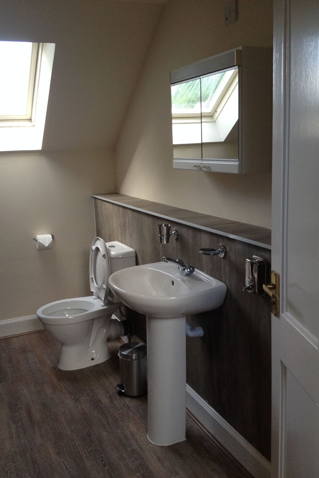 Une salle de bain comprenant des toilettes, un bidet et un lavabo, ainsi qu’un plancher en bois et une fenêtre située au-dessus des toilettes.